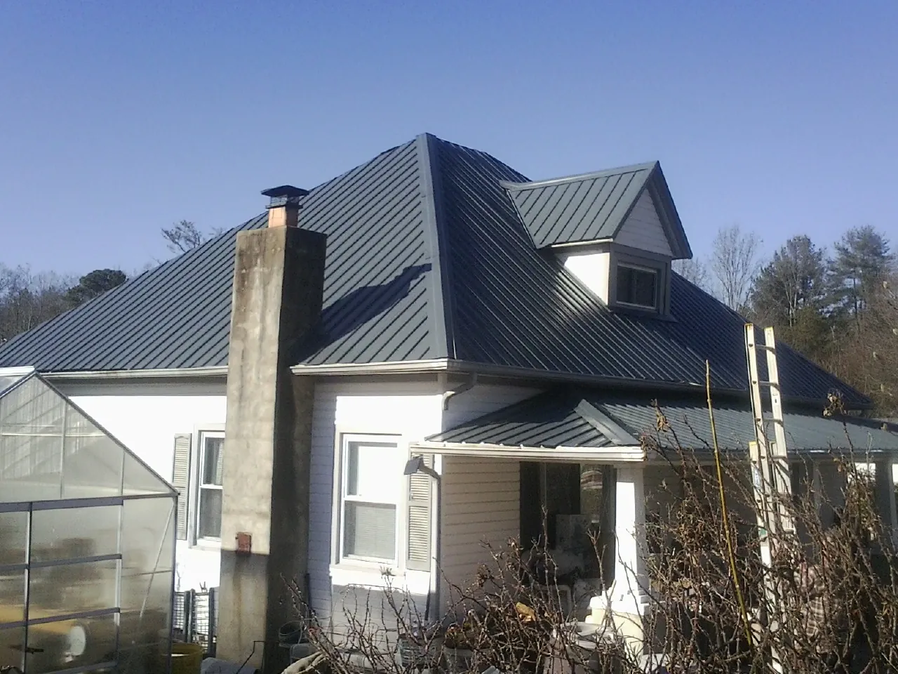 Dark blue standing seam metal roof on a white farmhouse with dormer — Slate & Tile Roof Repair by Roofing Brothers in Timnath