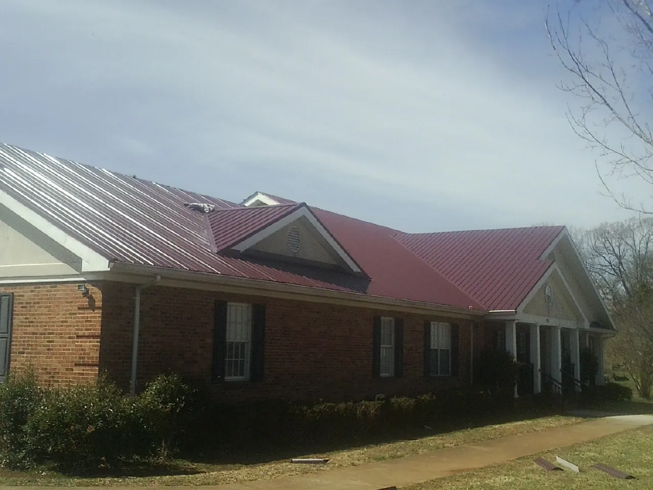 Red metal roof with gabled entries on a long brick building, from a Hail Damage Roof Repair job in Timnath
