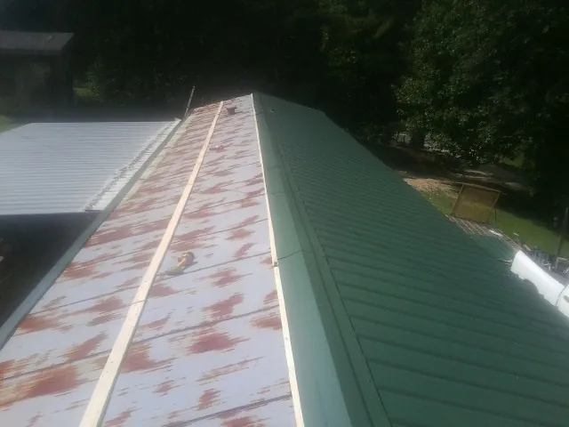 Old rusted panels beside newly installed green metal roofing — Wind Damage Roof Repair by Roofing Brothers in Timnath