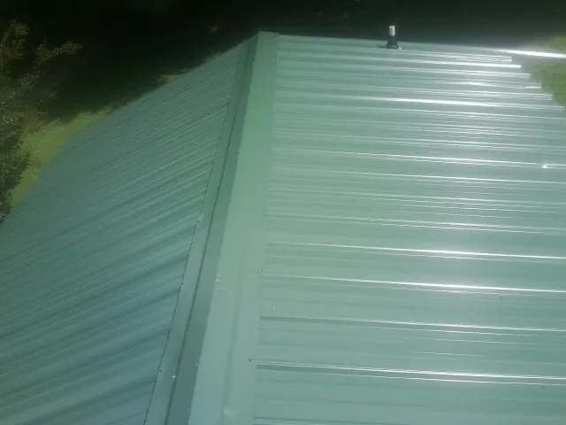 New green metal panels meeting at the ridge of a roof — Flat Roof Repair work by our crew in Timnath