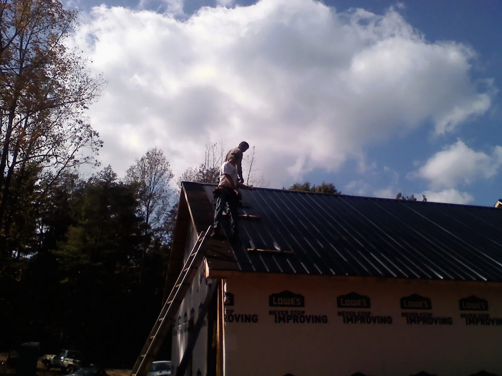 Roofer fastening dark metal panels high against a cloudy sky, from a Roof Inspection job in Timnath