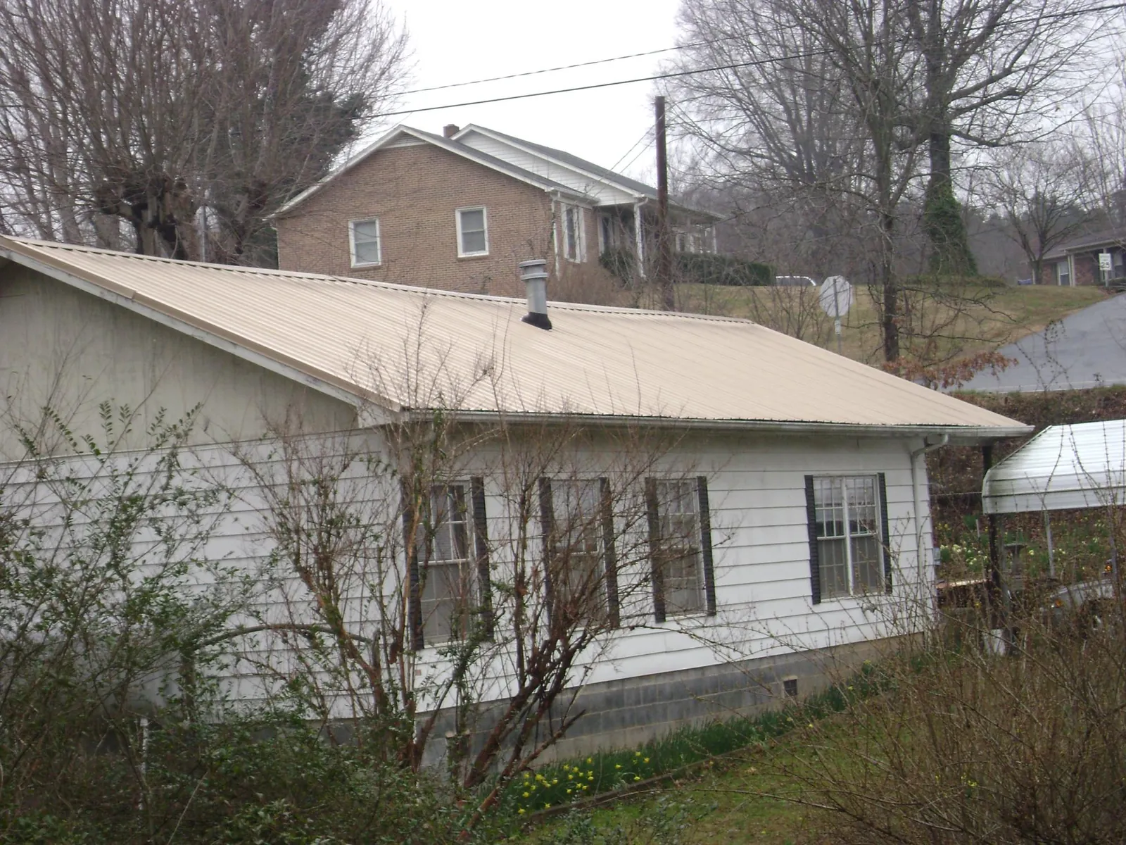 Tan metal roof on a white sided house set into a hillside — Commercial Roofing by Roofing Brothers in Timnath