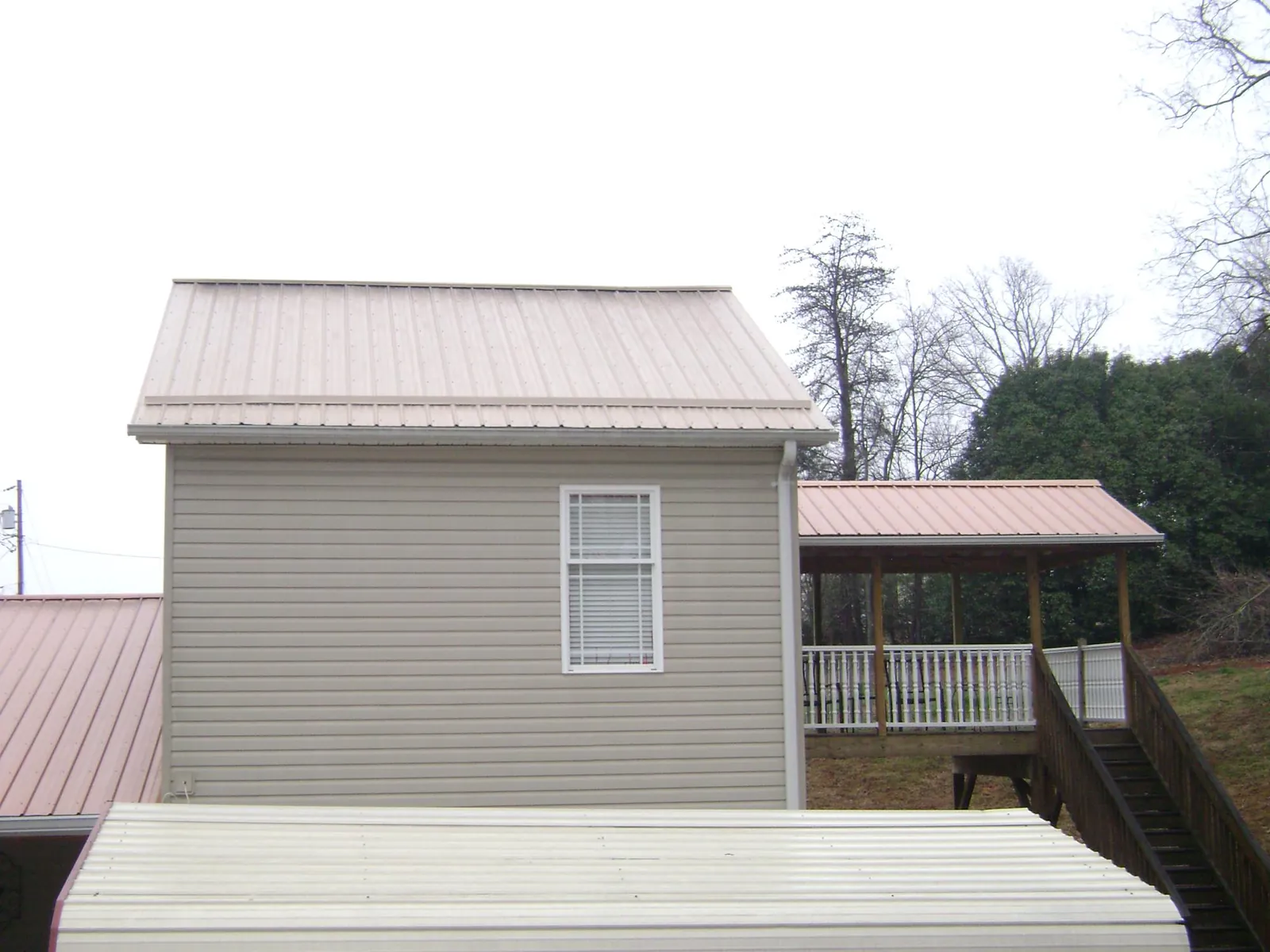 Tan metal roofs on a two story addition and attached porch, from a Roof Replacement job in Timnath